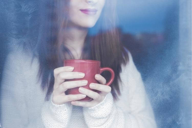 дівчина п'є каву біля вікна