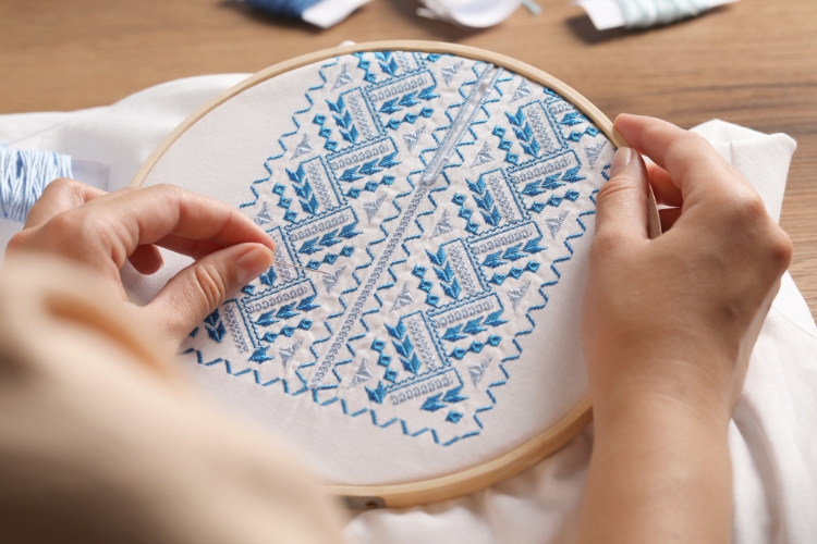 жінка вишиває сорочку на п'яльцях, блакитна вишивка